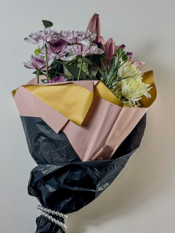 A beautiful bouquet of fresh flowers wrapped in elegant pink, gold, and black paper with pearl accents, symbolizing the natural inspiration and refined craftsmanship behind Debrovka’s handmade luxury leather sandals. This image reflects the brand’s dedication to artisanal quality, timeless style, and sophisticated design in every pair of sandals.